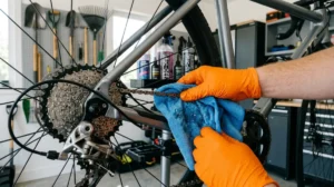 Mains gantées nettoyant une chaîne de vélo argentée avec un chiffon pour l'entretien mécanique.