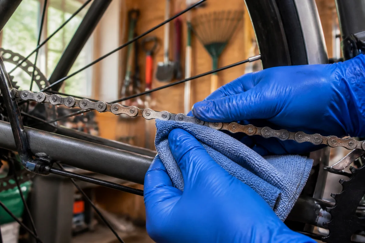 Mains gantées nettoyant une chaîne de vélo rouillée avec un chiffon pour illustrer comment enlever la rouille vélo.